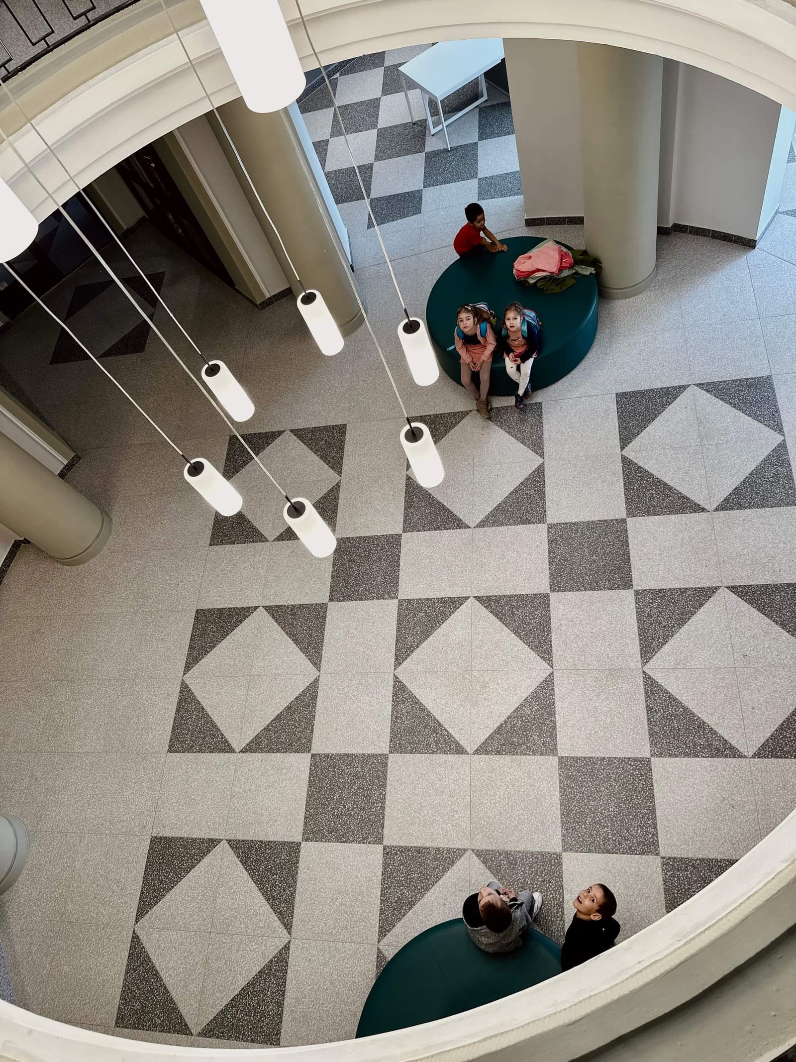 Komlói Múzeum — belső aula felülnézetből, terrazzo stílusú greslap padló háromszög-mintával, gyerekek üléseken
